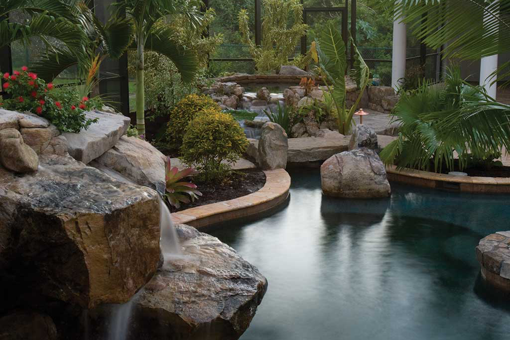 Lagoon pool and spa with spectacular grotto waterfalls and a stream connecting the spa to the pool, a natural stone bridge and tropical landscaping in Bradenton, Florida designed and built by Lucas Lagoons Inc.