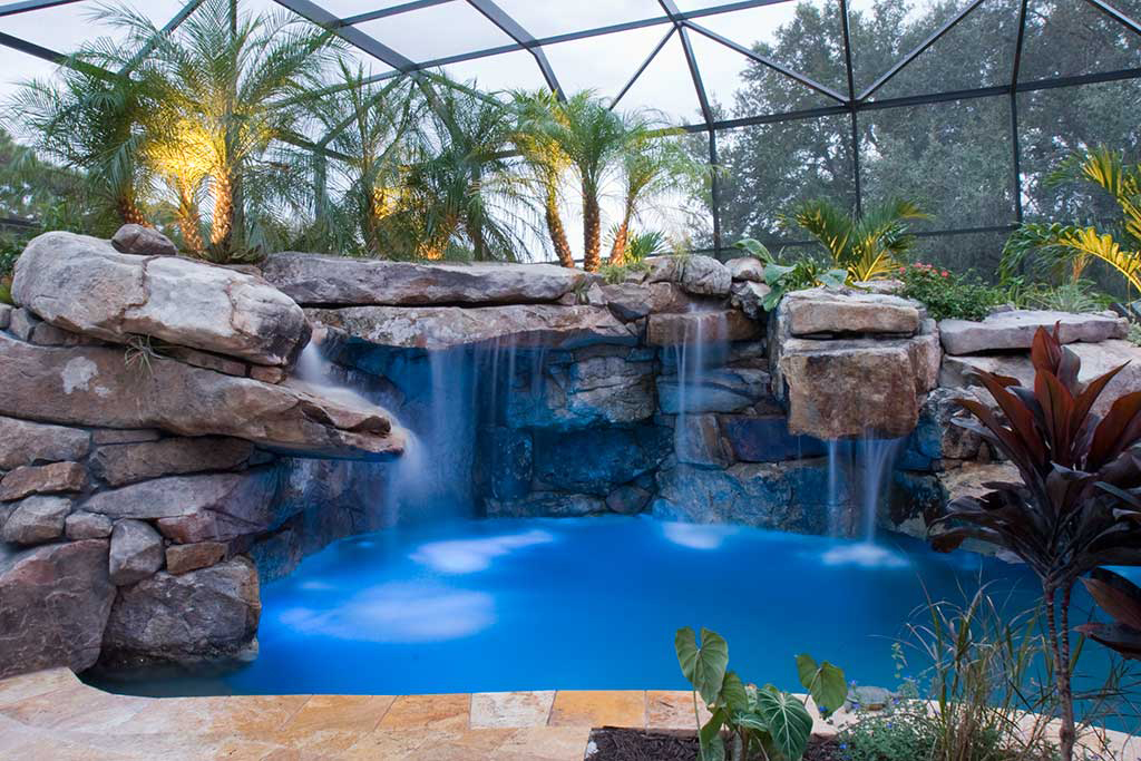 Lagoon pool and spa with spectacular grotto waterfalls and a stream connecting the spa to the pool, a natural stone bridge and tropical landscaping in Bradenton, Florida designed and built by Lucas Lagoons Inc.